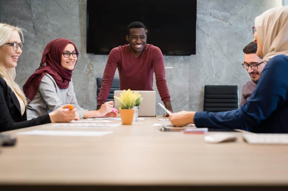 Communication, Training & OSHA - man in front of 4 other employees discussing safety and risk at a business meeting in a conference room